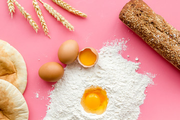 Ingredients for homemade bread. Bread near wheat ears, flour and eggs on pink background top view