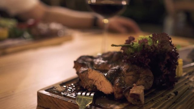Male hand holding wine glass at evening dinner in grill restaurant. Peole dinning grilled meat steak in barbeque restaurant.