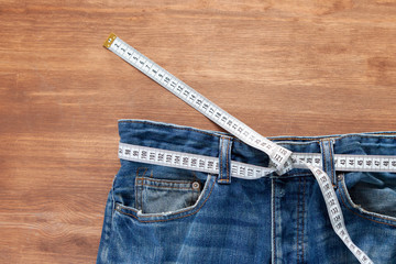 Jeans with a measuring tape on a green background. Weight loss concept
