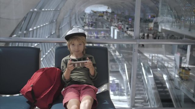 Cute child playing games, watching movie on smart phone in airport before departure. Using a portable handheld device traveling by airplane. Entertainment and online education on vacation