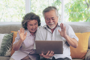 Senior couple using a laptop computer face time call to relatives descendant relatives grandchild, smiling feel happy in sofa at home - lifestyle senior concept