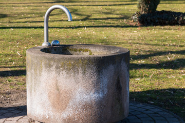 Naklejka na ściany i meble Concrete fountain with water dispenser in a park