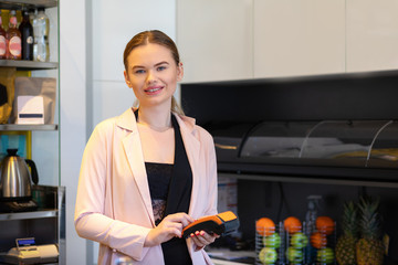 Smiling business owner standing at cash counter holding an electronic card payment machine 