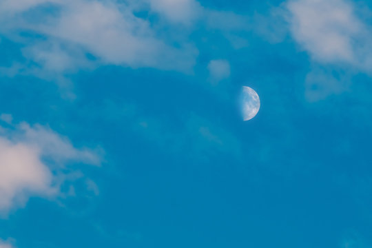 Half moon is seen in daytime, in blue sky with wispy clouds