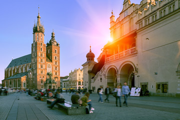 Market square and St. Mary's Basilica in Krakow, Poland in stunning sunset sun light. People tourists walking down the street and relaxing