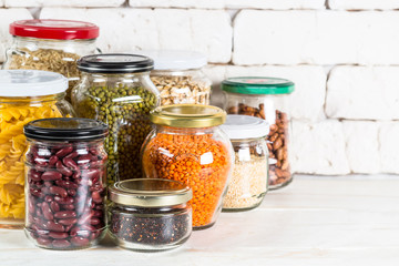 Cereals, Legumes, and beans in glass jars on white kitchen table. 