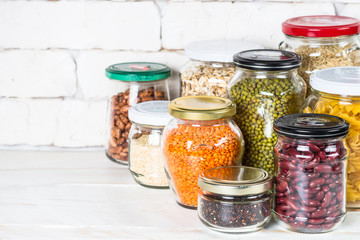 Cereals, Legumes, and beans in glass jars on white kitchen table. 