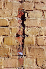 Cracked soft yellow paint, plaster surface on brick wall, grunge vertical shabby background detail close up