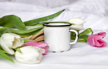 Fototapeta na wymiar mug, white and pink tulips, a book on a white sheet,