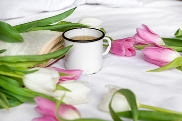 Fototapeta na wymiar mug, tea, white and pink tulips, a book on a white sheet