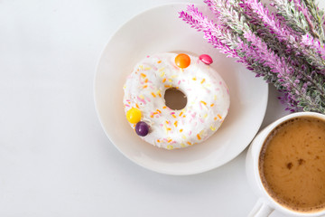 coffee mug with milk, pink lavender flowers,  donut with white icing on a plate, top view,