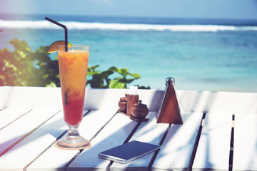 Cocktail and cellphone on the wooden table. Summer concept.