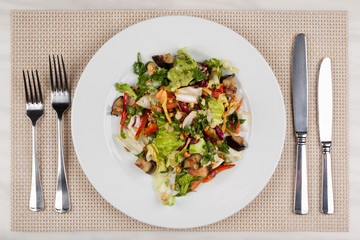 Eggplant salad with vegetables and walnuts and cutlery on a white plate.