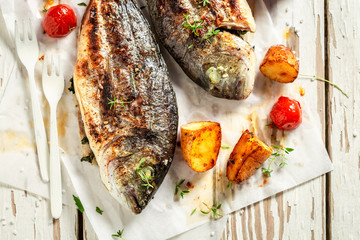 Homemade potatoes and seabream with tomatoes on white table