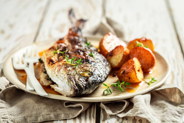 Potatoes and seabream with cherry tomatoes on white table