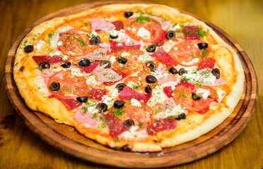 Pizza served with dill. Delicious hot pizza on wooden board plate. Food delivery service. Pizza with tomatoes black olives and ham. Take away food concept. Pizzeria restaurant. Italian pizza concept