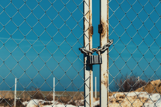 Padlock with chain on a metal gate with a metal grill. Against the blue sky