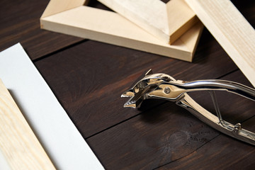 Stretching cotton canvas on wooden stretcher bar, steel canvas pliers on brown table
