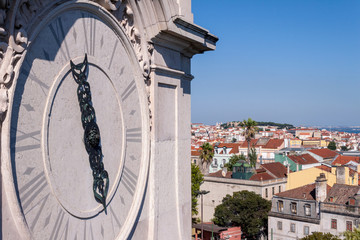 Close up of Gothic church tower clock with city views of Lisbon, Portugal in the back, on an sunny Summer afternoon. Concept for religion and Christianity/Catholicism.