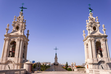 Imposing baroque towers of Monastery of Sao Vicente de Fora, with crosses and bells, as seen from the roof, in Lisbon, Portugal, at sunset, with blue pink skies, during a church visiting tour.