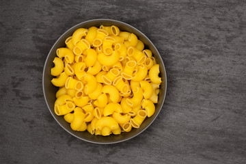 Lot of whole raw pasta pipe rigate variety in a grey ceramic bowl flatlay on grey stone