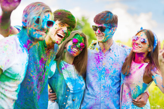 Cheerful and happy friends soiled by bright colorful paints making selfie and laugh on spring summer festival on nature. Company of young people having fun with holi paints. Holi party concept.