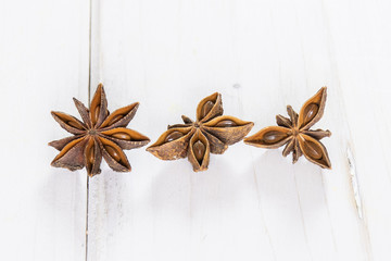 Group of three whole dry brown star anise fruit on white wood