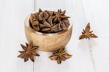 Lot of whole dry brown star anise fruit with wooden bowl on white wood