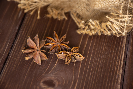 Group of three whole dry brown star anise fruit in a focus on jute cloth on brown wood