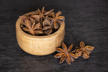 Lot of whole dry brown star anise fruit with wooden bowl on grey stone