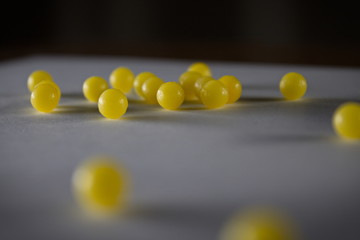 Dark soft focus close up of multiple small yellow balls candy bbs or pills on a gray paper with black background