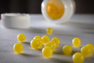 Soft focus close up of yellow round pills and bottle on white table