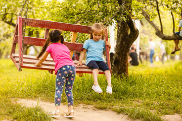 Fototapeta na wymiar Smiling little girl on a swing. Children playing outdoors in summer