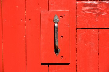 Einfacher Metall-Türgriff mit Vorhängeschloss an einem alten rot gestrichenen  holzbeplankten...