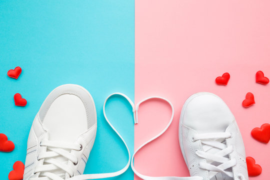 Heart created from white shoelaces between male and female sport shoes. Bright, red hearts. Love concept. Empty place for lovely, cute text, quote or sayings on pastel blue and pink paper. Closeup.
