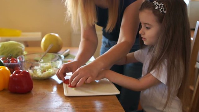 Children's creative in the kitchen. Mom and daughter put a funny face in the kitchen while cutting salad. The girls are laughing