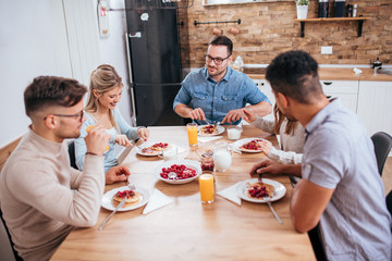 Five young people enjoying meal while sitting at the dinning table in the homely kitchen.