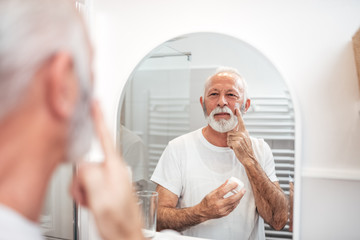 Senior man applying cream in the bathroom.