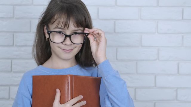 Schoolgirl nerd. Smart young girl with glasses with a book. Happy child with a book.