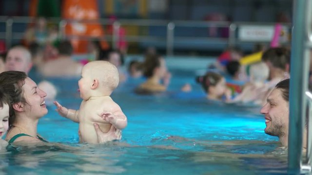 Happy baby swimming in the pool with their parents. The child is happy and joyfully tongues out