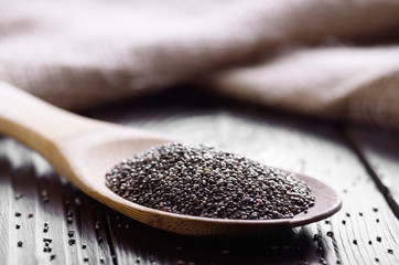 Raw Chia seeds in bamboo spatula on wooden table