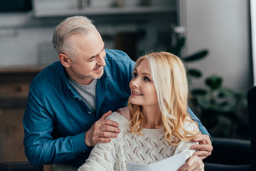 happy husband embracing cheerful wife at home