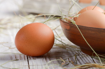 Raw organic brown chicken eggs in clay bowl on white kitchen wooden table