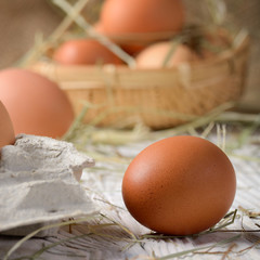 Raw organic brown chicken eggs in square wicker basket on white kitchen wooden table