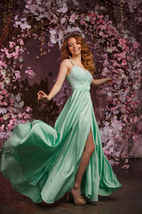 Beautiful woman model in a mint-colored dress on a flowered spring background. Beauty girl with a stunning makeup and hairstyle.