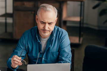 Fototapeta premium tired man looking at laptop while holding glasses