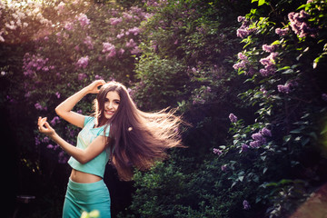 Wonderful spring. A beautiful young girl enjoys nature and sunlight among the blossoming lilac.