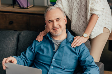 Fototapeta premium cropped view of woman standing near cheerful husband with laptop
