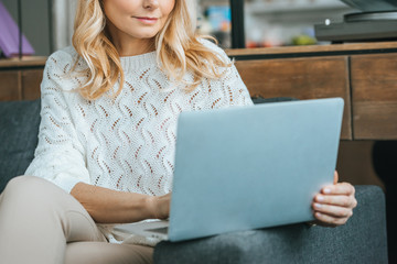 cropped view of woman with blonde hair using laptop at home