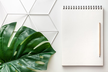 White empty notebook with space for your text on a geometric pattern. Copy space, mockup. Decoration from the green leaf monstera. Top view hipster desk.